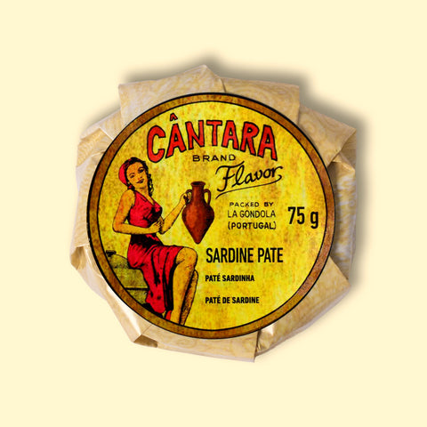 A round tin of sardine pâté in a glossy paper wrap with an illustration of a woman in a red dress beneath Cântara written in red lettering