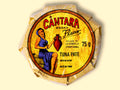 A round tin in a glossy paper wrap with a woman on the front in a blue dress holding a container of olive oil beneath the Cântara logo in red.