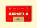 Red box of Carmelo Spicy Mussels on a wooden surface. The box is bright and has four small illustrations, a glass of wine, a book, a suitcase and a pair of glasses.