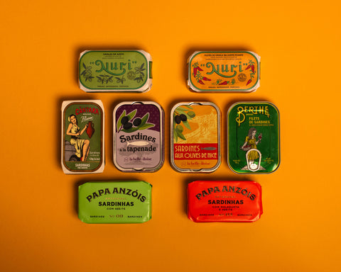A selection of colourfully-packaged tinned sardines and mackerel against a yellow background.