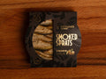 Smoked sprats in pistachio oil, shown in partially open black packaging, with the golden-brown fish visible inside. 