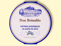 A round tin with a white card wrap. The cover has a blue and gold border. Don Reinaldo is written in gold lettering below a drawing of the cannery.