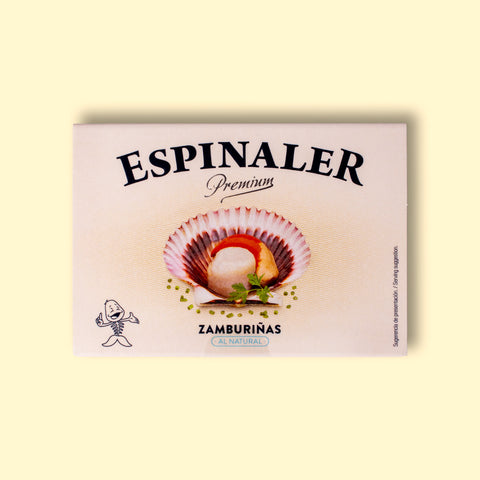 A cream-coloured rectangular box with an open variegated scallop in its shell on the front, beneath Espinaler written in black lettering. The tin is on a pale wood background.