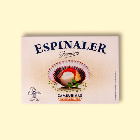 A cream-coloured rectangular box with an open scallop in its shell on the front, beneath Espinaler written in black lettering. The tin is on a pale wood background.