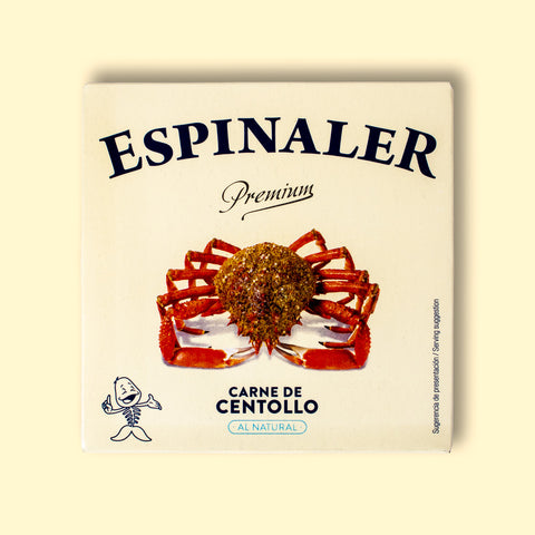 A tin of spider crab meat in square-shaped, cream-coloured card packaging with a picture of a 10-legged spider crab beneath the Espinaler logo in blue lettering. The can is against a pale yellow background.