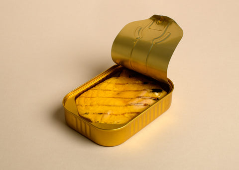 An open tin of salmon with griddle stripes on the fish. The tin is gold against a white background. The lid is open but still attached to the tin.