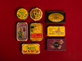 A selection of colourfully-packaged tinned sardines, mackerel, tuna, squid and sardine and mackerel pâtés against a red background.