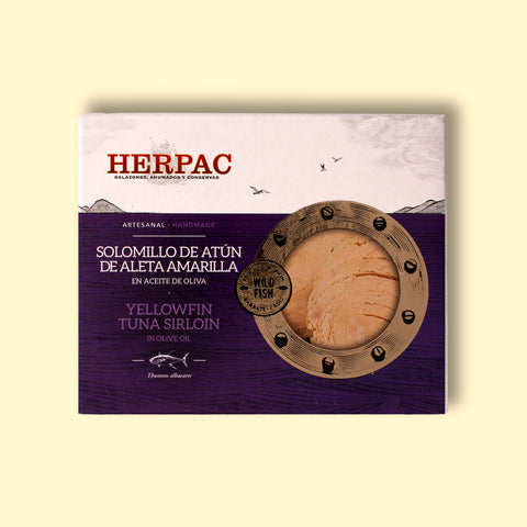 A tin of yellowfin tuna sirloin in rectangular card packaging. The Herpac logo is written in red lettering above a purple sea with seagulls flying over it. There is a golden porthole on the right hand side of the packaging through which you can see the light peach coloured tuna sirloin.