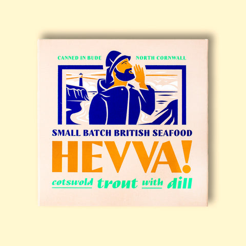 Box containing Cotswold trout with dill from Hevva! The box is illustrated with a fisherman calling out over the Cornish coast with cliffs and a lighthouse in the background. The box is colourful with Hevva! written in golden, embossed letters