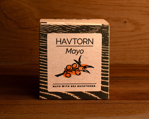A tin of mayonnaise with buckthorn in light grey square card packaging with blue borders, featuring an illustration of a buckthorn.