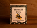 A tin of mustard spread with dill in light grey square card packaging with blue borders, featuring an illustration of a dill flower.