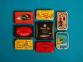 A selection of colourfully-packaged tinned mussels, sardines, tuna and mackerel against a blue background.