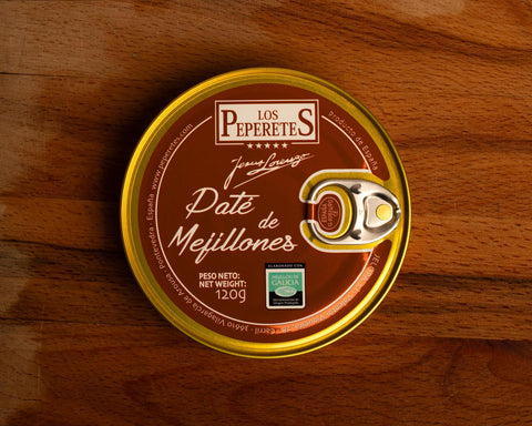 A circular tin of mussel pâté with a gold-coloured border, a silver ring pull, and a reddish brown label with the Los Peperetes logo at the top and pate de mejillones written in white lettering beneath it.