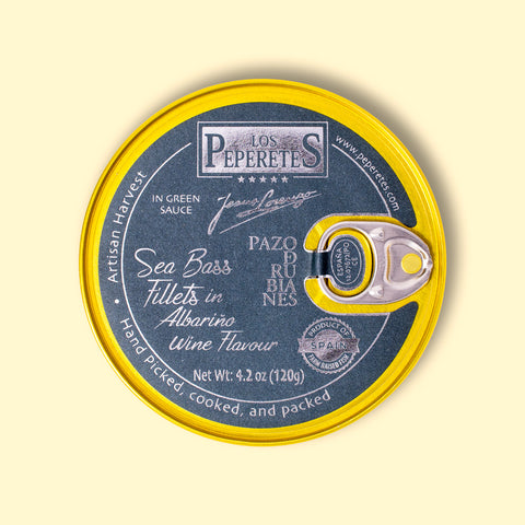 Sea bass in salsa verde with albarino wine, packaged in a circular black tin with golden corners and silver lettering, against a wooden backdrop.