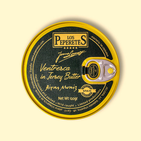 Ventresca in jersey butter, packaged in a circular chocolate-brown tin with a golden border and golden lettering, against a wooden backdrop. 