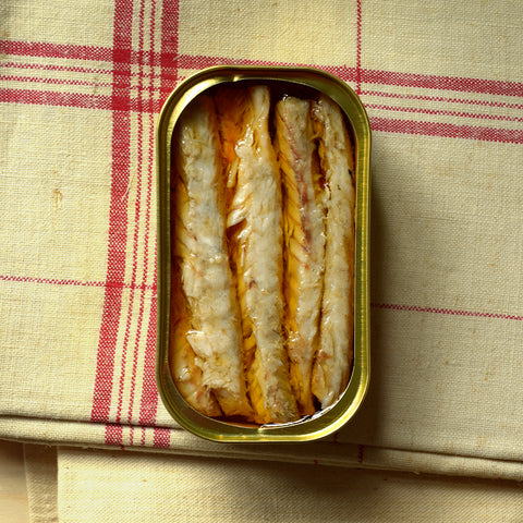 Mackerel fillets carefully placed in a gold-coloured tin resting on top of a cream cloth with red checks.