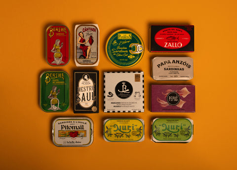 A selection of colourfully-packaged tinned sardines, mackerel, tuna, squid and mussels against a yellow background.