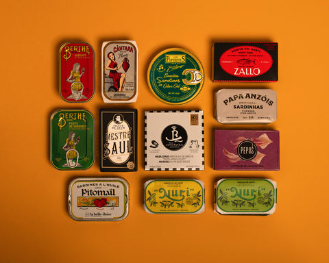 A selection of colourfully-packaged tinned sardines, mackerel, tuna, squid and mussels against a yellow background.
