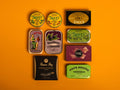 A selection of colourfully-packaged tinned sardines, mackerel, tuna, squid and sardine pâtés against a yellow background.