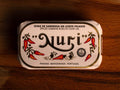 A tin of spicy sardine roe in white and gold paper packaging with illustrations of red chillies beneath the Nuri logo. 