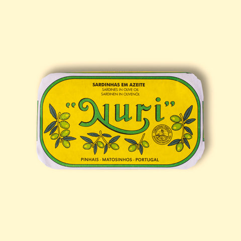 A tin of sardines in a yellow paper wrap with a green and white border. Nuri is written in green lettering above some small olive branches.