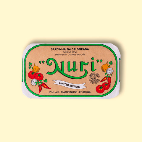 A paper-wrapped tin of Nuri sardines with the Nuri logo in green lettering against beige background, and images of chillies, tomatoes, onion and coriander either side of the log.