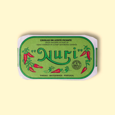 A tin of spicy mackerel in a green paper wrap with a white border. Nuri is written in green lettering above some red chilli peppers.