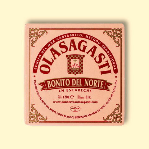 A tin of Bonito del Norte tuna in pink packaging with red lettering and an ornate gold border, against a wood background