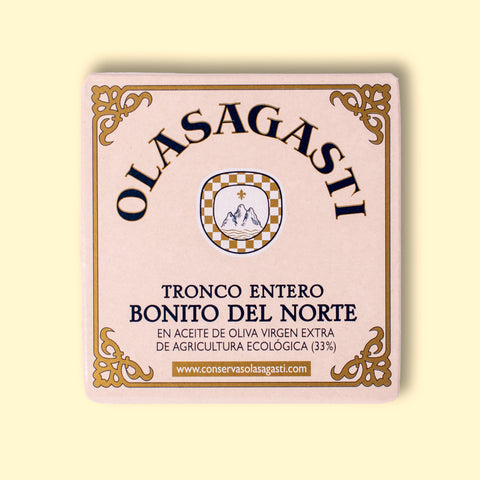 A square tin of tuna with an ornate gold border and Olasagasti written in black lettering against a pale pink background