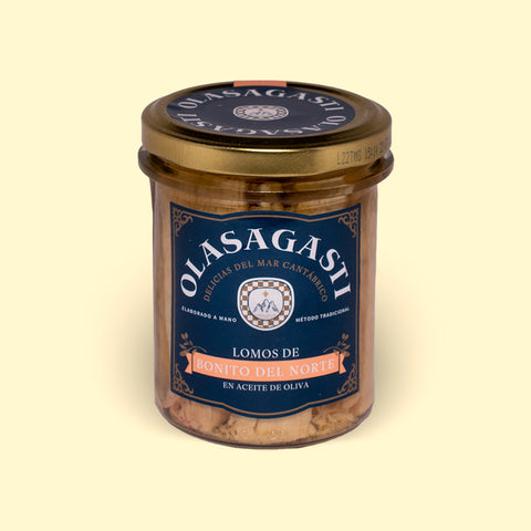 A closed jar of tuna fillets with a gold lid and a blue label with Olasagasti written in white lettering, against a pale yellow background