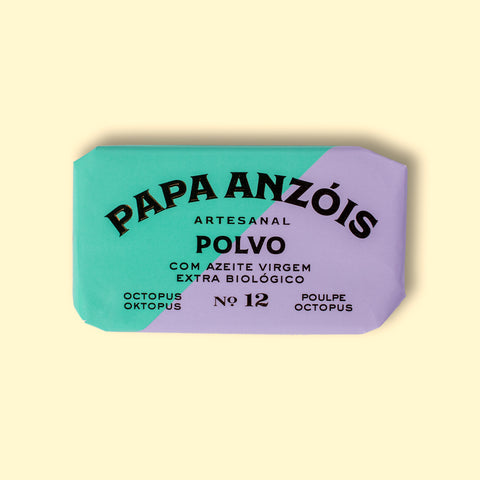 A rectangular tin of octopus in extra virgin olive oil with green and pale lilac paper packaging against a yellow wood background. 