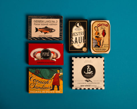 A selection of colourfully-packaged tins of
Cornish sardines, salmon, scallops, mackerel and tuna against a blue background.