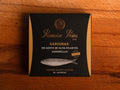 Spicy sardines in black and gold card packaging. Ramón Peña is written in gold lettering above a silver-grey image of a sardine.