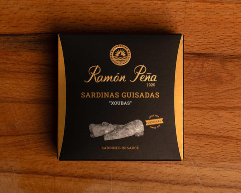 A tin of small sardines in black and gold packaging. Ramón Peña is written in gold lettering above a silver grey image of a sardine