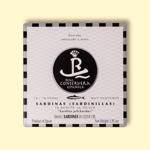 A tin of small sardines in black and white card packaging with a black and silver chequered border, against a wood background.