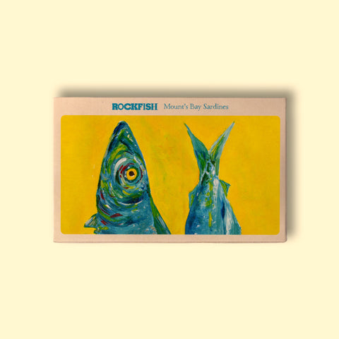 A tin of sardines in off-white card packaging with a painting of a brightly coloured blue, green and yellow sardine head and tail against a vivid yellow background. The painting is beneath Rockfish Mount's Bay Sardines written in blue lettering.