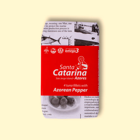 A tin of tuna with pepper, in newspaper packaging with a red band around it with Santa Catarina written in white lettering on it.