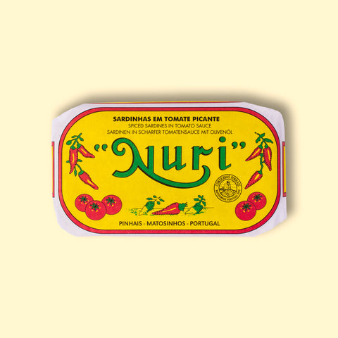 A tin of sardines in spicy tomato in a yellow paper wrap with a white and red border. Nuri is written in red above images of tomatoes and red chilli peppers.