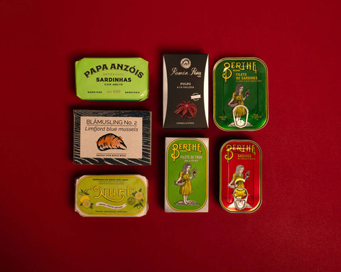 A selection of colourfully-packaged tinned tuna, sardines, mackerel, herring and octopus against a red background.