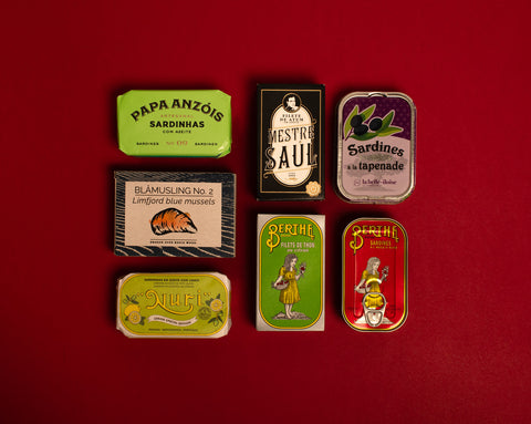 A selection of colourfully-packaged tinned mussels, sardines and tuna against a red background.