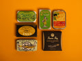 A selection of colourfully packaged tins of sardines and tuna against a yellow background.