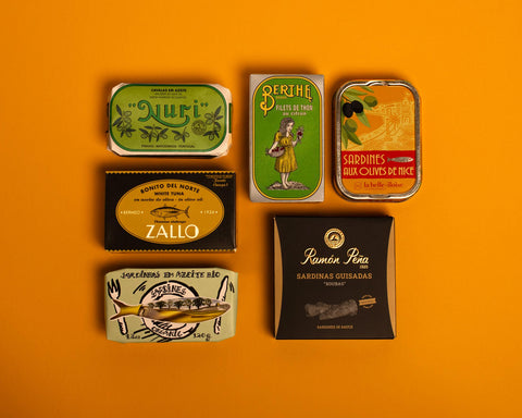 A selection of colourfully packaged tins of sardines and tuna against a yellow background.