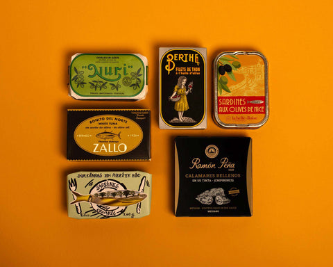 A selection of colourfully packaged tins of sardines and tuna against a yellow background.