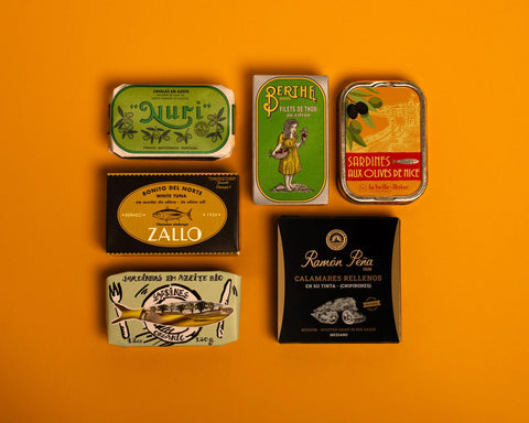 A selection of colourfully packaged tins of sardines and tuna against a yellow background.