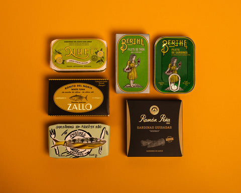A selection of colourfully packaged tins of sardines and tuna against a yellow background.
