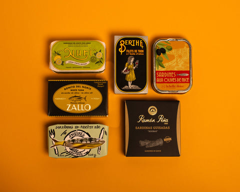 A selection of colourfully packaged tins of sardines and tuna against a yellow background.