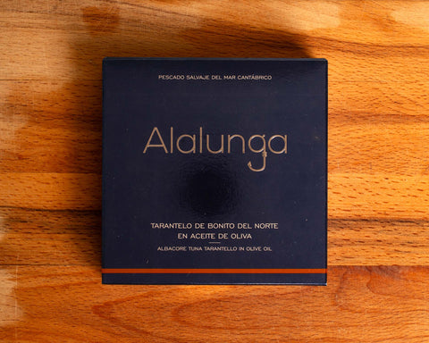 anned white tuna in square blue card packaging with Alalunga in silver, embossed lettering above a diagram of a tuna. There is a copper stripe along the bottom of the packaging.