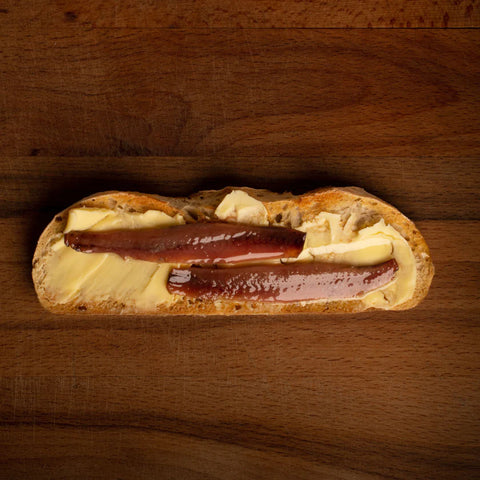 Mouthwatering tinned anchovies on toasted bread with butter, on a dark wooden backdrop.