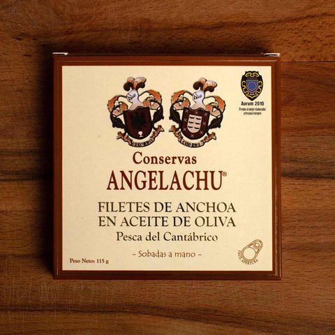 A large square tin of anchovies in a rectangular brown and cream box against a wood background