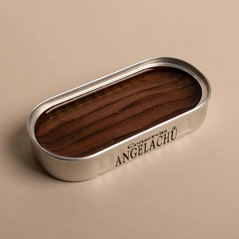 An open tin of anchovies with brown anchovy fillets in olive oil inside and conservas Angelachu written on the side of the silver tin.